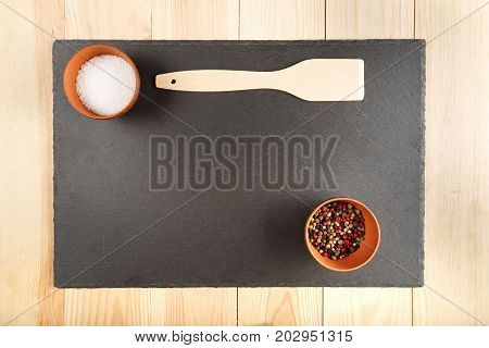 multicolored peppers peas and salt in a clay cup on a slate board wooden kitchen spatula top view