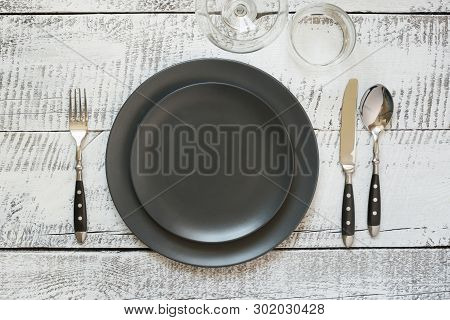 Table Place Setting With Black Plate On White Wooden Table. Top View.