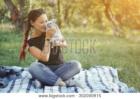 Asian Woman Took On Picnic Little Gray Bunny. Happy Girl Hugging Bunny In Green Summer Forest. Girl 