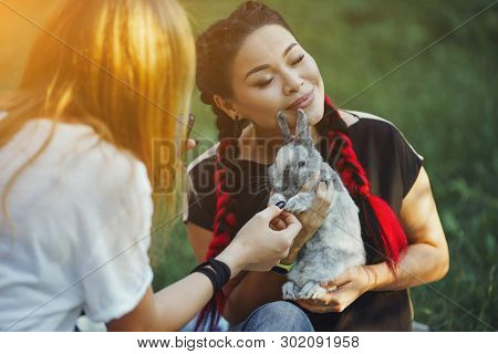 Young Woman With Red Konekalons Huggs A Rabbit On Nature. Beautiful Portrait On Green Grass Backgrou