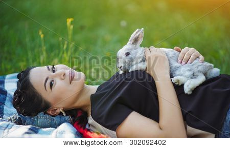 Young Asian Hugging Rabbit On Green Grass. Lovely Summer Picnic. Girl Laying On Grass.