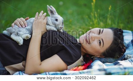 Beautiful Asian Woman Laying On Green Grass With Fluffy Rabbit Smiles To Camera. Corean Girl Having 