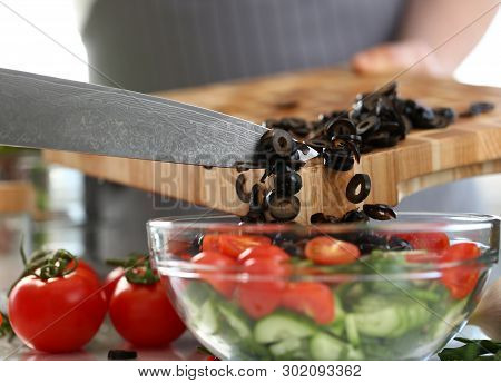 Chef Pouring Round Pieces Black Olive Salad Bowl. Man Chopping Vegetable On Wooden Cutting Board At 