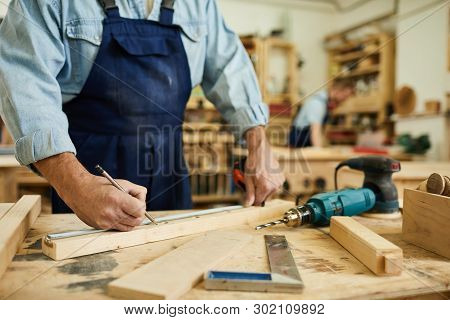 Close Up Of Mature Carpenter Working With Wood Standing At Table In Workshop, Copy Space