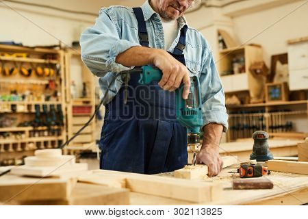 Mid Section Portrait Of Mature Carpenter Drilling Wood While Working In Joinery, Copy Space