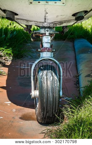 Old Small Single Engine Airplane Landing Gear On Grassy Overgrown Parking Pad.