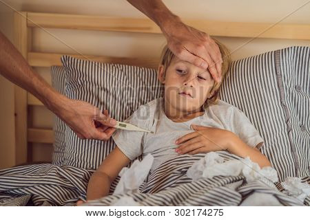 Sick Boy With Thermometer Laying In Bed And Father Hand Taking Temperature. Father Checking Temperat