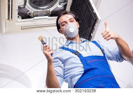Young repairman repairing ceiling air conditioning unit 