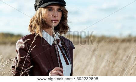 Portrait Of Attractive Female Model In Leather Jacket And Fashionable Cap Looking At Camera Against 