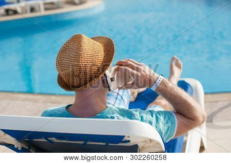 Man Lying On A Lounger And Talking On A Phone Near The Pool