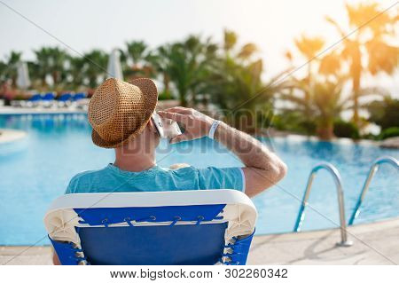 Man Lying On A Lounger And Talking On A Phone Near The Pool
