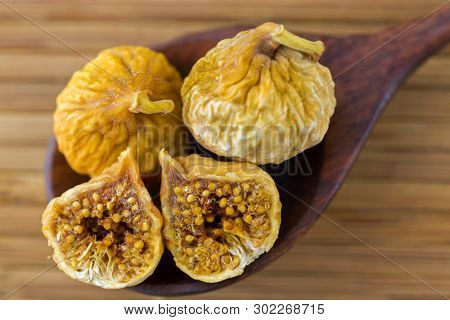 Dried fig fruit cut in half showing seeds on dark wooden spoon on wood background 