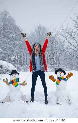 Funny Snowman In Stylish Hat And Scarf With Funny Girl On Snowy Field. Happy Girl Plaing With A Snow