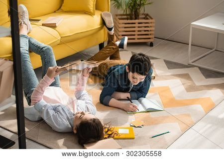 Adorable Kids Lying On Floor At Home And Doing Schoolwork Together