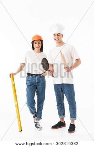 Full length portrait of a young attractive woman architect and man chef standing isolated over white background, holding building level and rolling pin