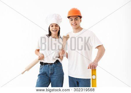 Portrait of a young attractive man architect and woman chef standing isolated over white background, holding building level and rolling pin