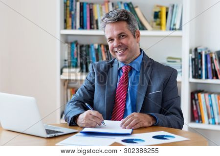 Laughing Mature Businessman Working At Desk At Office Of Company