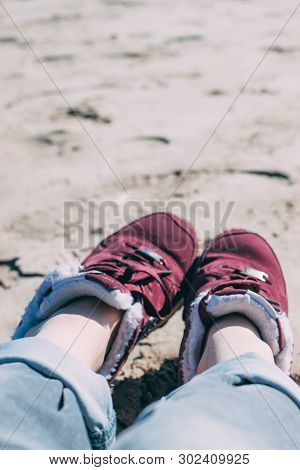 Feet Of Young Woman In Sport Footwear And Jeans Relaxing After Hiking On Sand Beach. Pov. Adventure 