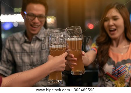 Group Of Asian Friends Holding Pint Glass Of Beer Toasting For Drink On Friday Night In Relaxing Aft