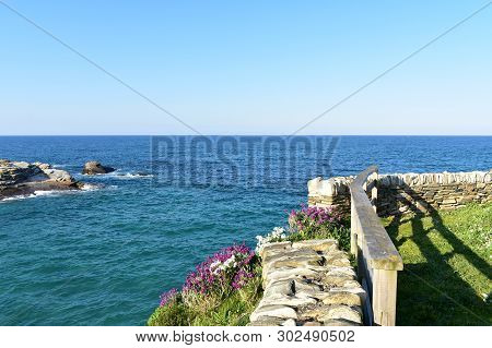 Coast With Grass, Flowers And Viewpoint With Stone Wall And Wooden Handrail. Blue Sea, Sunny Day, Ri