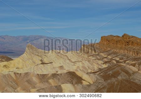 Bands Of Colored Rock At Zabriskie Point In Death Valley, California.  Blue Sky With Wispy White Clo