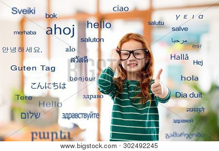 education, translation and learning concept - smiling red haired student girl in glasses and green striped shirt over greeting words in different foreign languages on background
