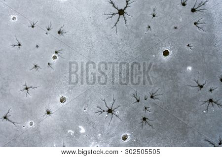 An Aeiral Drone Looking Down Captures Holes And Cracks In Frozen Lake Ice. Dark And Dusty Water Bene