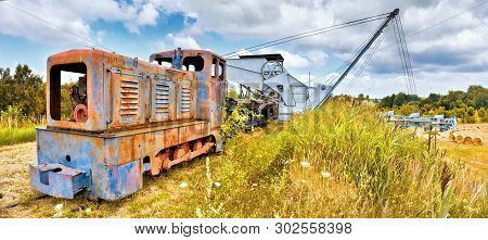 Old Rusty Locomotive And Bucket Chain Excavator And A Row Of Coal Vagons On A Grass Hill Outdoors In