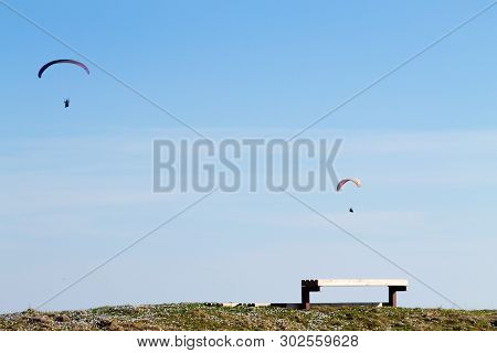 Paraglider On Blue Sky With Empty Bench On Foreground