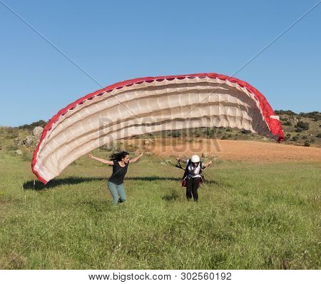 Female Pilot Landing With A Paraglider In The Field With A Blue Sky Background