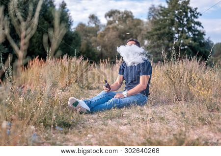 Modern Man Is Resting In Nature And Vaping And Letting Off Steam From An Electronic Cigarette. Vapin