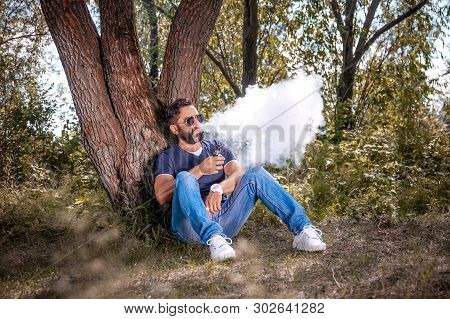 Confident Vaper Blows Up A Couple An Vape On The Forest Floor. Electronic Cigarette Concept.