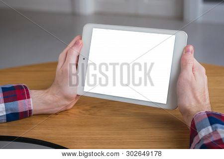 Man Sitting At Wooden Table And Looking At Digital Tablet Computer Device With White Blank Screen. M