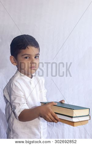 Back To School Concept. Cute Middle Eastern Boy Holding A Stack Of Books Against The White Backgroun