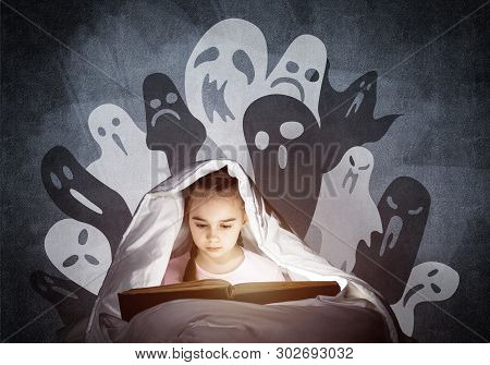 Engrossed Little Girl Reading Book In Bed Before Going To Sleep. Kid In Pajamas With Flashlight Hidi