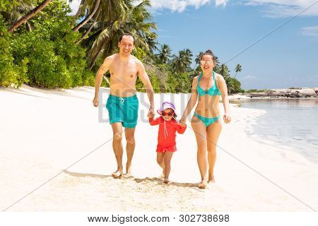 Portrait Of A Smiling Young Family Walking On The Sandy Beach
