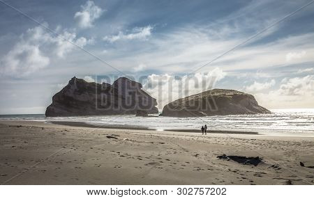 A Couple Walking Hand In Hand Exploring Wharariki Beach. Wharariki Beach Is West Of Cape Farewell, T