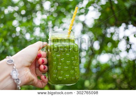 woman's hand holding a jar with green cold-pressed juice, nature background. Healthy eating, detoxing, juicing, body cleancing concept 