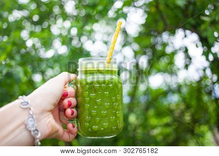 woman's hand holding a jar with green cold-pressed juice, nature background. Healthy eating, detoxing, juicing, body cleancing concept 