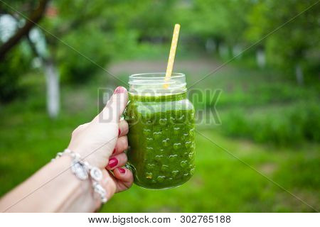 woman's hand holding a jar with green cold-pressed juice, nature background. Healthy eating, detoxing, juicing, body cleancing concept 