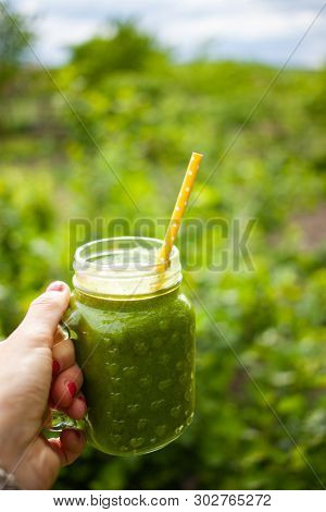 woman's hand holding a jar with green cold-pressed juice, nature background. Healthy eating, detoxing, juicing, body cleancing concept 