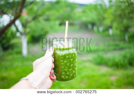 woman's hand holding a jar with green cold-pressed juice, nature background. Healthy eating, detoxing, juicing, body cleancing concept 