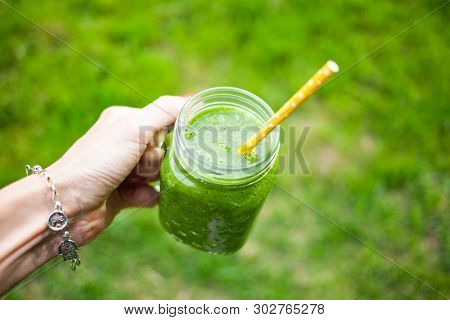 woman's hand holding a jar with green cold-pressed juice, nature background. Healthy eating, detoxing, juicing, body cleancing concept 