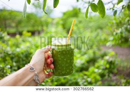 woman's hand holding a jar with green cold-pressed juice, nature background. Healthy eating, detoxing, juicing, body cleancing concept 