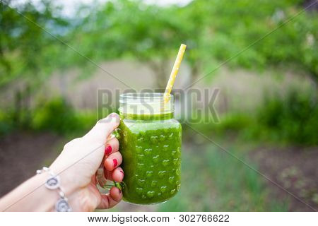 woman's hand holding a jar with green cold-pressed juice, nature background. Healthy eating, detoxing, juicing, body cleancing concept 