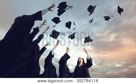 A Group Of Graduates Throws Hats Up Into The Sky.