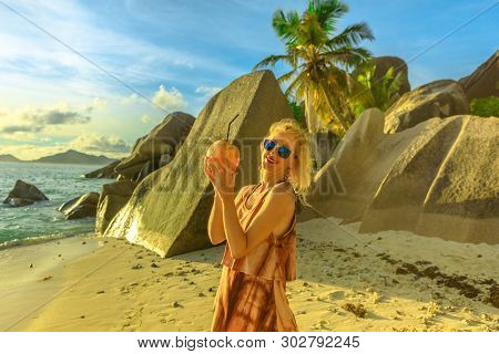Woman Holding A Coconut Drink At Anse Source Dargent, La Digue, Seychelles. Huge Boulders And Palm T