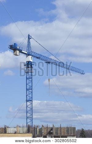 Construction crane blue near the unfinished building on the background of the cloudy sky. Construction of a multi-storey residential building. Construction of a modern office center