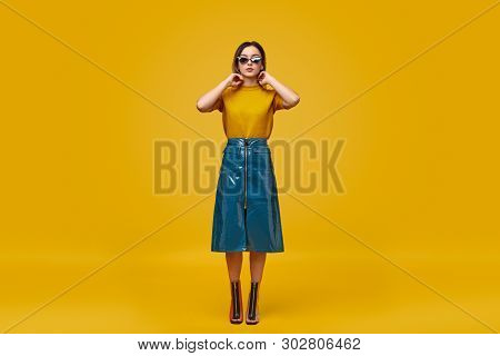 Full Length Young Female In Trendy Cyberpunk Outfit Touching Neck While Standing Against Yellow Back