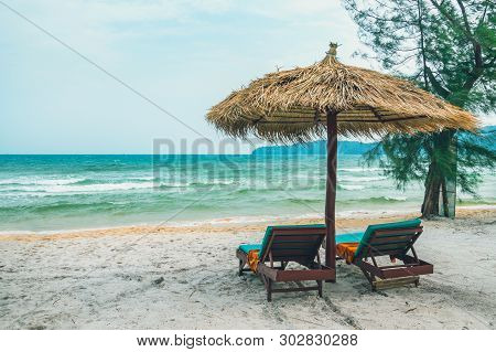 Two Chaise Lounges And Straw Umbrella On Tropical Beach. Coast Of Island Koh Rong Samloem, Cambodia.